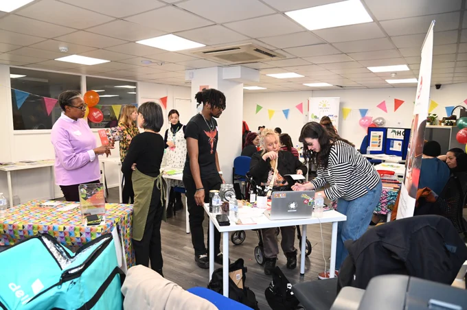 Lots of people chatting in a bright room with tables, displays, and bunting