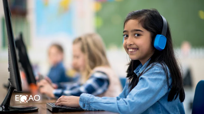 Student wearing headphones using a computer in a classroom setting, with other students in the background. Logo 'EQAO' visible on the image.