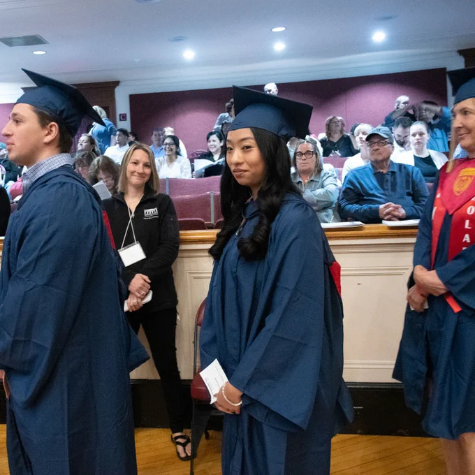 people in caps and gowns stand in line in auditorium