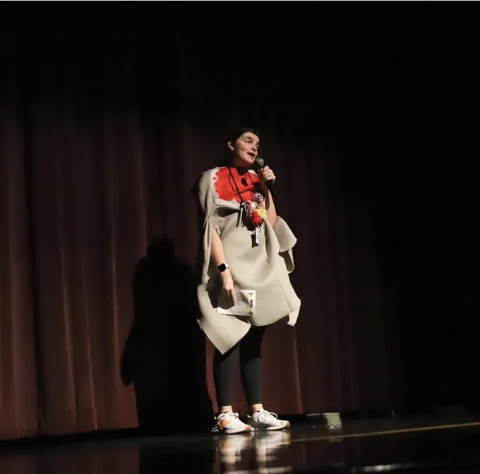 Amanda on the stage during a stage night in the theatre being an MC in a shark costume and holding a mic.