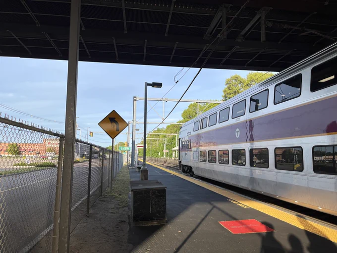 MBTA Commuter Rail train stopped on a low-level platform. A Market Basket is seen in the distance.