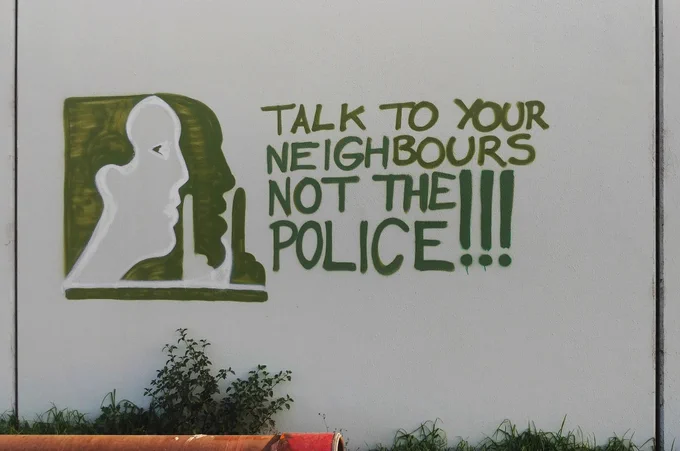 "Talk to your neighbours, not the police!"
Mural parodying the 'Neighbourhood Watch' logo.