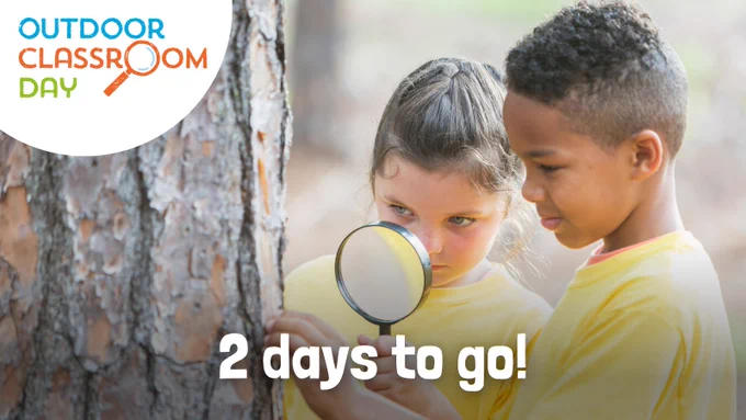 A graphic featuring an image of two children using a magnifying glass to examine a tree trunk during an outdoor lesson. The words '2 days to go!' are written in white along the bottom of the image, and the Outdoor Classroom Day logo is overlaid in the top left corner.