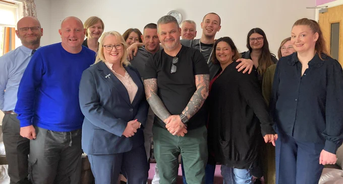 Drugs and Alcohol Policy Minister Christina McKelvie  wearing a dark blue jacket with a large group of staff and service users at Crossreach's Residential Recovery Service in Glasgow.