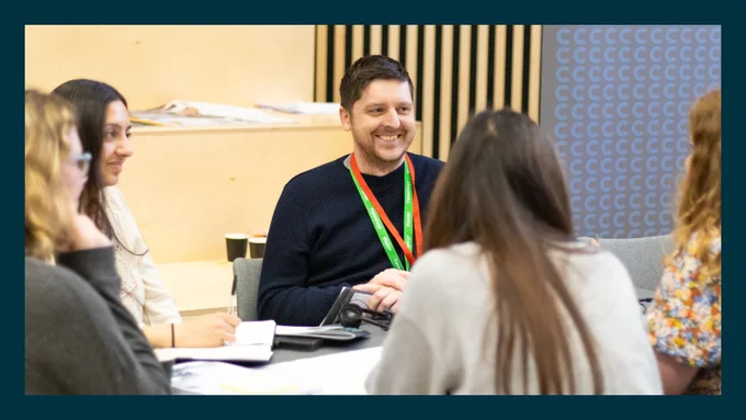 A man is at a table with others around him. He's smiling. 
