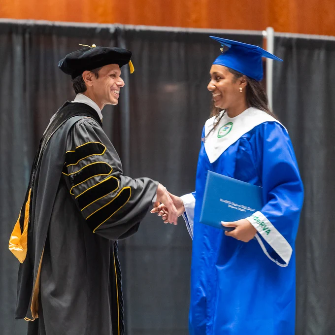President Rao, in black and gold graduation robes, shakes a graduating student's hand.