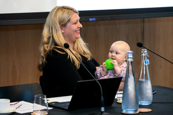 A mother and her baby at RCS England. The mother is sitting on a panel, with the baby in her lap.
