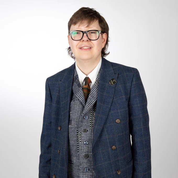 Our brilliant Theo: a young man looking dapper in his glasses and three piece suit. 
