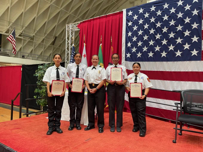 Chief Crowley standing with 4 students holding graduation certificates on a stage/platform