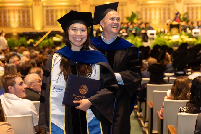 Two School of Medicine Class of 2024 graduates in regalia walking up the Soldiers and Sailors Memorial Hall auditorium aisle, smiling after receiving their diplomas.  