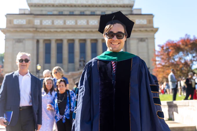 A School of Medicine Class of 2024 graduate in regalia smiling with his family outside of Soldiers and Sailors Memorial Hall.  