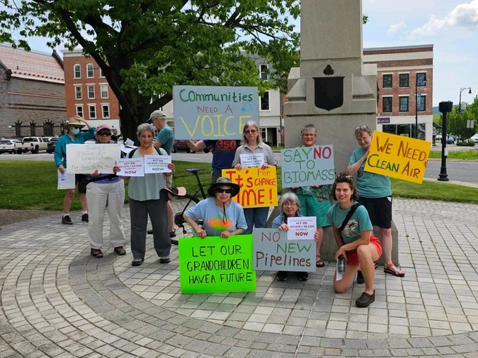 A group of people with signs calling for climate action around a monument in a town square. 