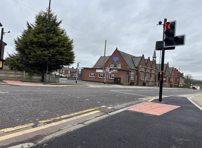 This shows the elongated island with the one traffic pole with the one green man control box. It shows the red tactile paving and the lack of red tactile paving on the dropped kerb where it meets the road. This is not safe or accessible and is down right dangerous.