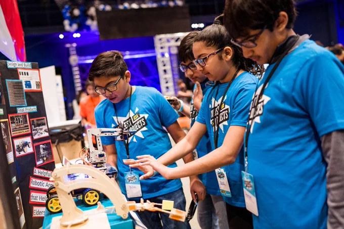 Four young creators in their Coolest Projects blue t shirts looking at their hardware project.
