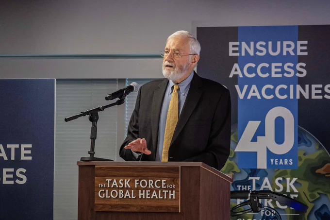 A person speaks at a podium during an event celebrating 40 years of The Task Force for Global Health, with banners emphasizing the importance of global access to vaccines.