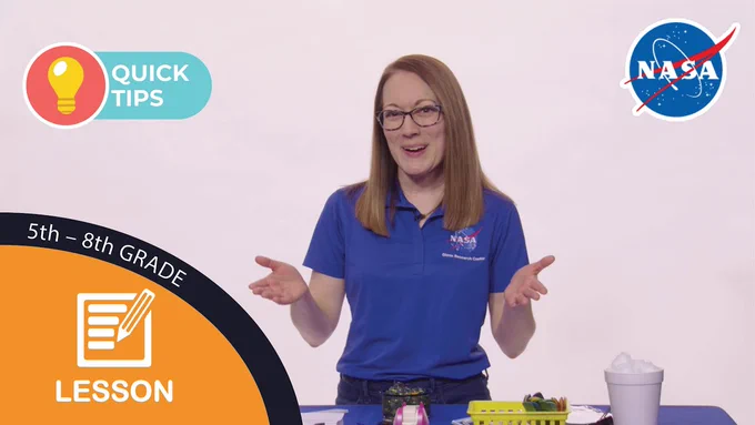 Screenshot of the Safe Landing on the Lunar Surface activity demonstration video. A woman wearing a blue NASA polo shirt smiles while standing near a table filled with supplies for the activity she is about to demonstrate. 