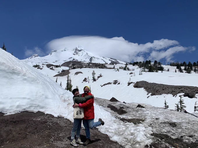 Sam and Chen are hugging, with Sam’s foot up like in the princess diaries movie where Anne Hathaway is like “if it’s real love I gotta put my foot up” anyways behind them is like a big giant snowy Portland mountain it’s actually called Mt Hood and people ski there but Sam and Chen did not ski they just frolicked a little and took photos