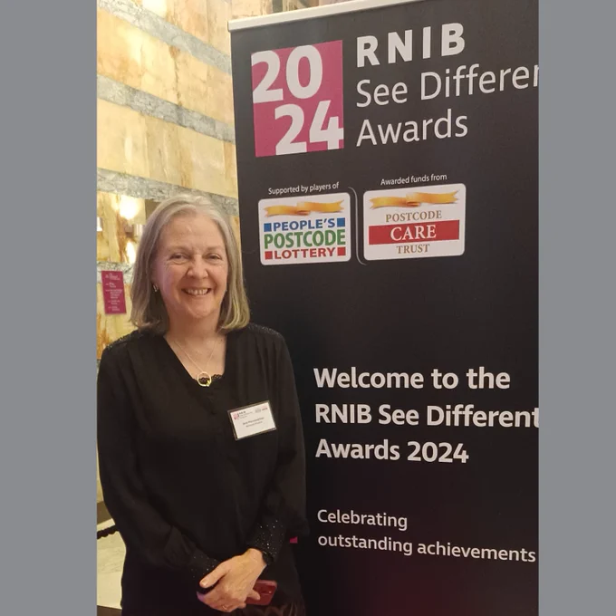 Dr Jane Macnaughton standing next to a banner for the RNIB See Different Awards 2024, which is supported by players of People's Postcode Lottery and Postcode Trust. Banner reads welcome to the RNIB See Differently Awards, celebrating outstanding achievements.