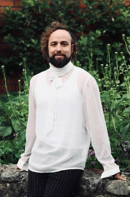 Writer Daf James stands against a wall in the community garden at Chapter Arts Centre