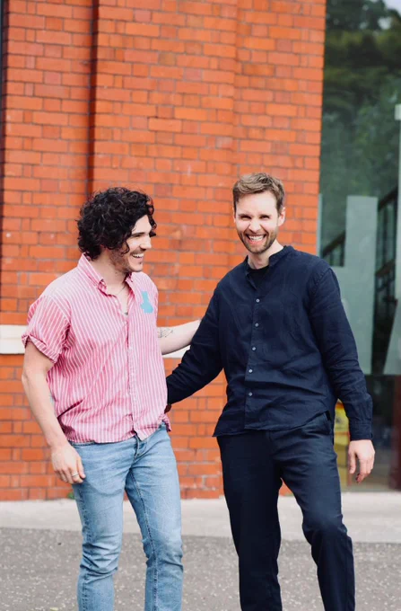 Actors Fra Fee and Sion Daniel Young standing outside Chapter Arts Centre. They are both laughing.
