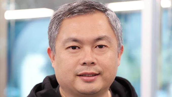 A picture of UC Davis MBA alum Larry Liu smiling and wearing a black sweatshirt in front of a light background.