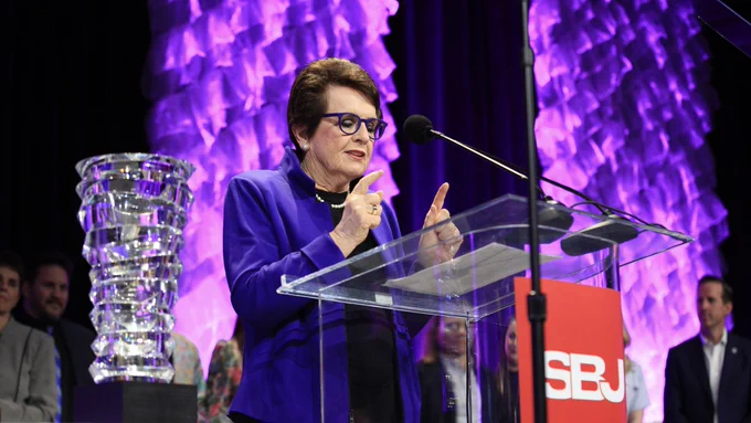Billie Jean King giving an acceptance speech on stage after the PWHL was announced as the award winner. Beside her, the award sits on a platform.