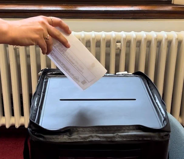 A person placing a ballot paper into a ballot box at a polling station.