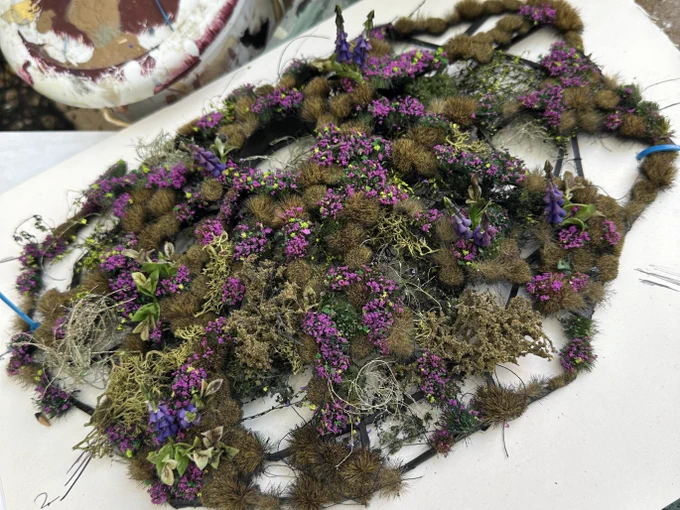 A miniature version of the Yorkshire Moors consisting of green grass and purple and pink wild flowers, sits on a piece of paper surrounded by sketches.