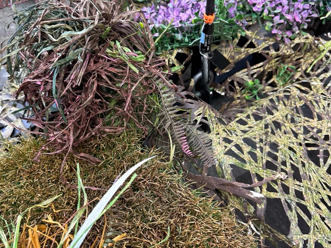 Green, orange and purple reeds and netting are pictured on a grey floor. 