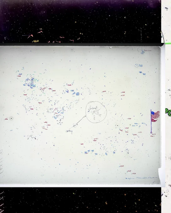A wide view of the entire photographic glass plate negative of the night sky. The stars tiny appear black against the clear white areas of space, like grains of sand scattered on a piece of paper. Then, there are two different people who have added hundreds of identifying numbers and measures in two different hands and in blue, violet, red, and black ink.