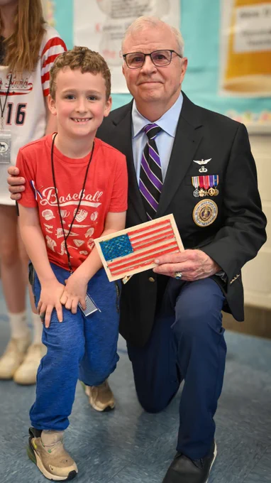 Veteran with medals posing with student with arm around shoulder holding a homemade flag