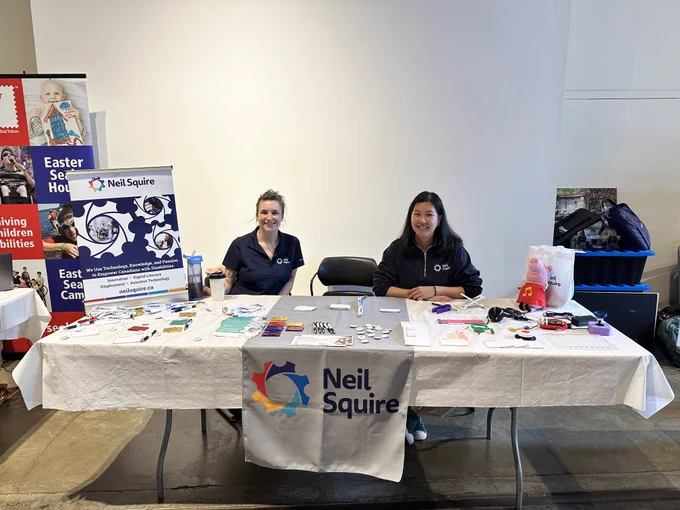 Eden and Kristina at the Neil Squire booth at the Abilities Expo with brochures and assistive technologies on display.