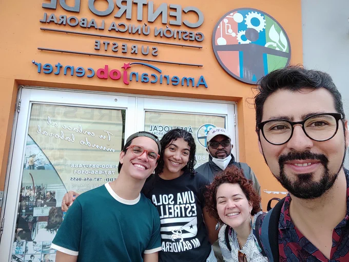 A selfie of Manuel and four others standing in front of the doors to an orange building.