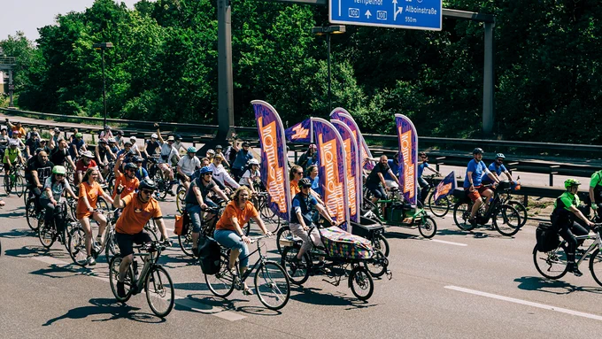 Foto von einer Sternfahrt in Berlin: Viele Menschen fahren mit dem Fahrrad über die Autobahn. Im Vordergrund fahren Personen mit Lastenrädern, auf denen Flaggen mit der Aufschrift "Zeit für die RADvolution" befestigt sind.