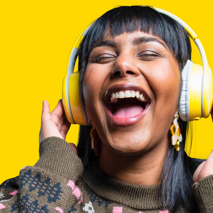 Close up image of woman enjoying listening to music through yellow headphones. 