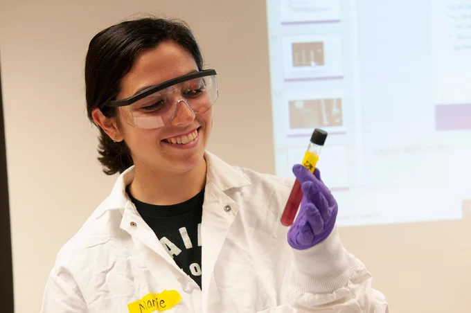 A student in PPE holds up a vile and smiles