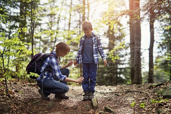 A parent spraying bug spray on a child in the forest