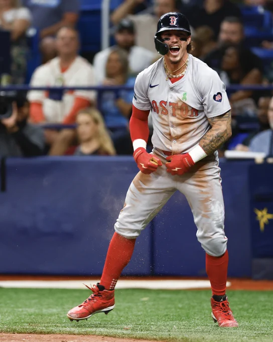 Jarren Duran flexes as he celebrates after crossing home plate. He wears a dirty road gray Red Sox uniform with red lettering.