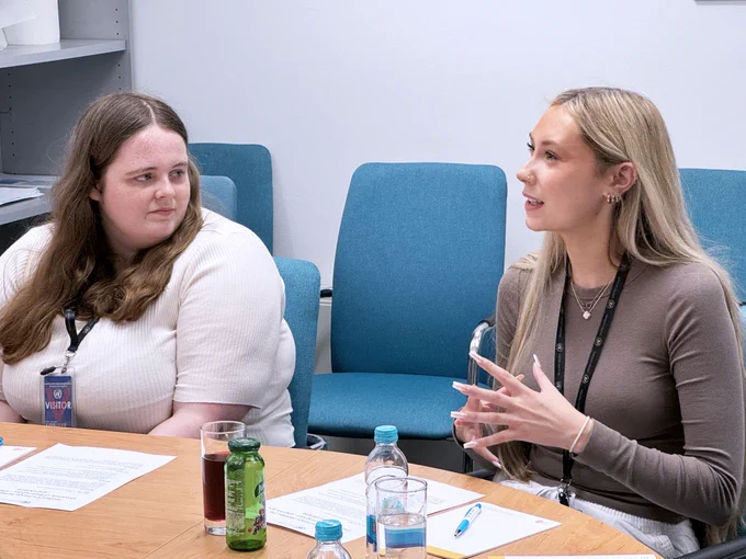 two girls at the meeting, one is speaking while the other listens. 