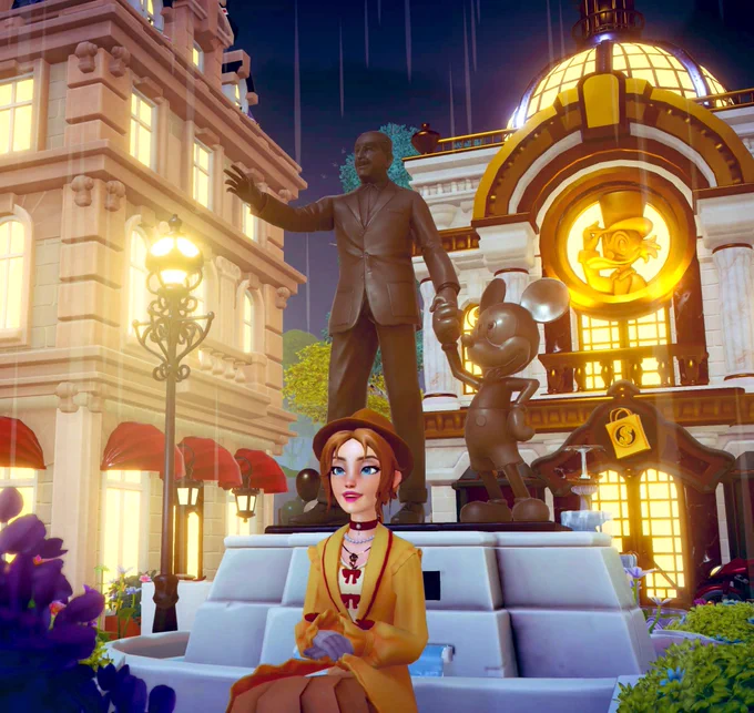 Disney Dreamlight Valley screenshot of a player avatar sitting on a bench in front of the Partners Statue which features Walt Disney and Mickey Mouse, located in a setting with buildings in the background.
