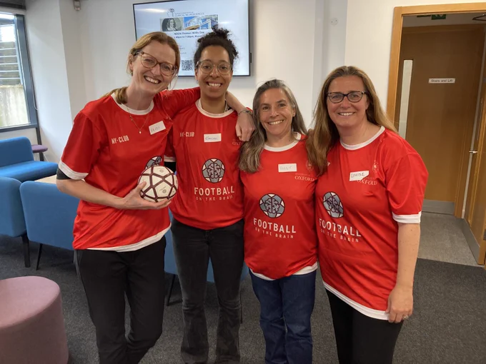 Four women in red Football on the Brain shirts pose together smiling for the camera