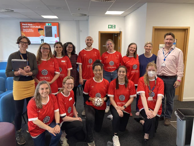 Group of people pose smiling at camera, most in red "Football on the Brain" shirts