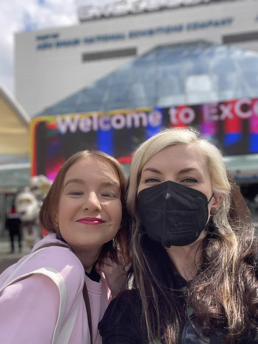 Lyssa and Zoë taking a selfie in the sunshine, with the ExCel centre behind them.
Lyssa is wearing pink lipstick and a light pink sweatshirt.
Zoë is wearing a green top and black blazer.