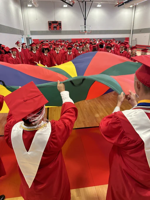 Several graduates playing with a colorful parachute.