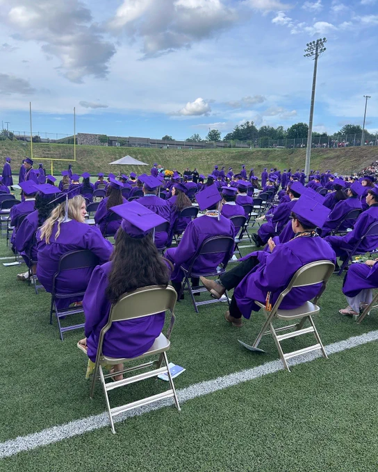 Graduates sitting in chairs on the football field during the ceremony.