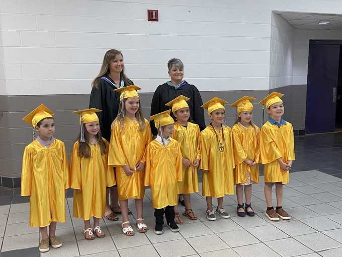 Eight elementary students in yellow caps and gowns with two principals.