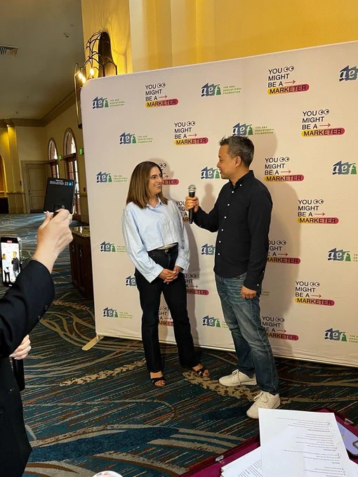 marisa being interviewed in front of a backdrop by a man in a black shirt at an event