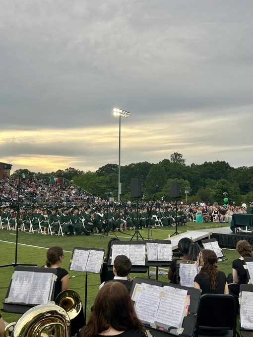 Graduates sitting in chairs on the football field facing the stage.