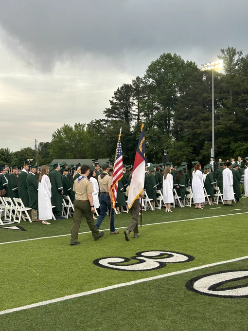 Boy Scouts walking with flags down the aisle on the football field.