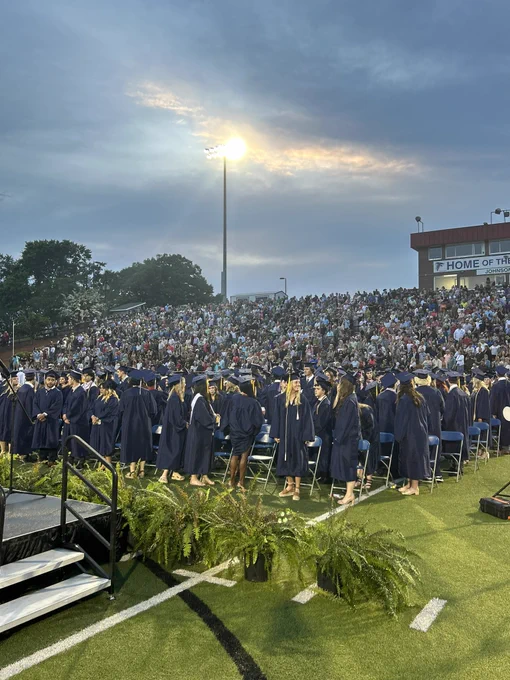 Graduates standing at their chairs on the field.